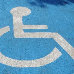 Biały symbol osoby na wózku inwalidzkim namalowany na niebieskiej nawierzchni.